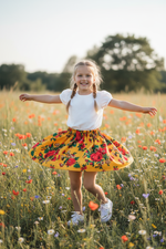 Little girl twirling in a vibrant golden yellow Polish folk peony skirt in a sunny garden